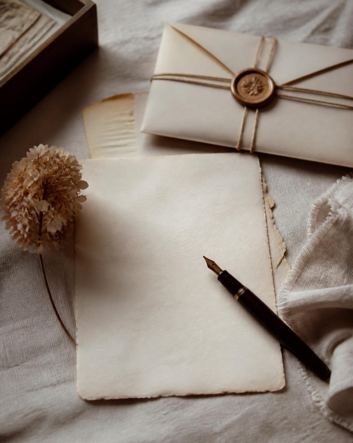 A warm flat-lay of handwritten stationery, a fountain pen, a folded letter, wax seal, and twine on soft linen